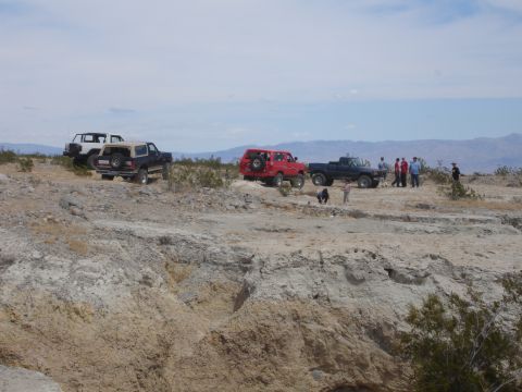 1996 Ford Bronco - Several off-road vehicles are gathered in a desert landscape under a cloudy sky.