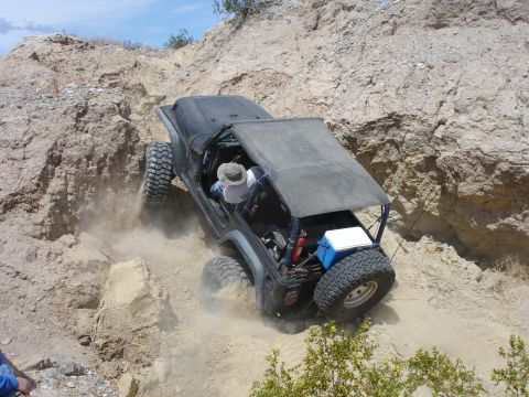 1996 Ford Bronco - A Jeep navigates a steep, off-road path, kicking up dust as it climbs.