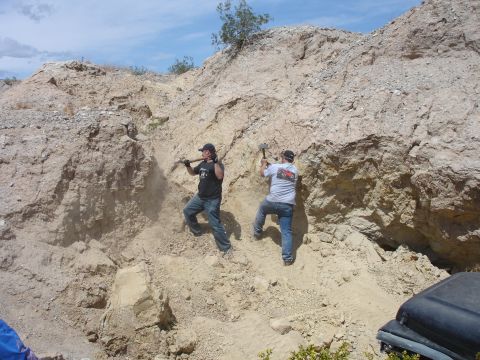 1996 Ford Bronco - Two men are digging into a dirt hillside with pickaxes, with a portion of a black vehicle visible in the foreground.