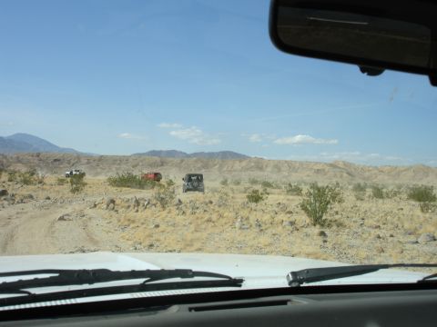 1996 Ford Bronco - Multiple SUVs traverse a dusty desert trail under a clear blue sky.