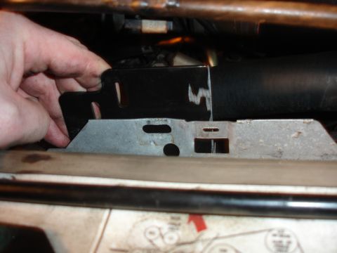 1996 Ford Bronco - A hand manipulates a black metal bracket near a silver bracket and a black hose.