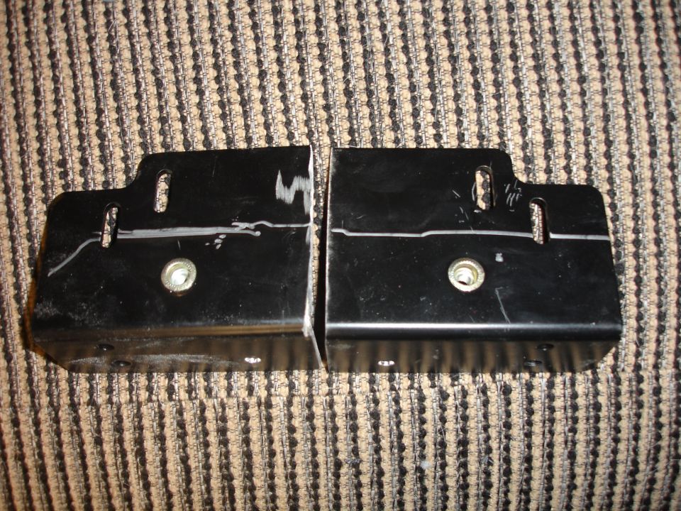 Two black metal brackets with bolt holes and scratch marks, lying on a striped fabric surface