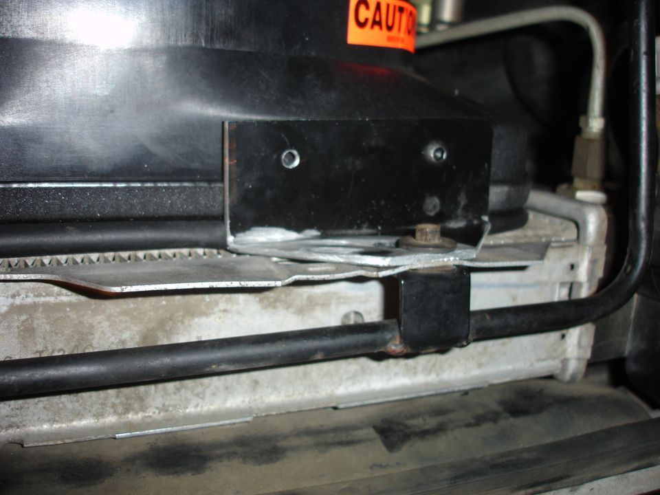 Close-up of bracket and hoses at a truck radiator core support with caution decal