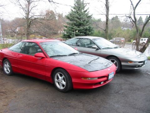 1996 Ford Probe - Two Ford Probes are parked side-by-side on a wet driveway under a cloudy sky.