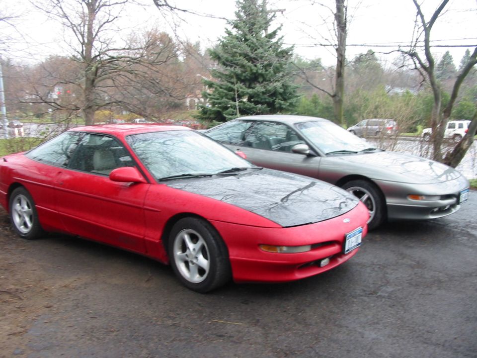Two Ford Probes parked outside, one red with a black hood, the other silver