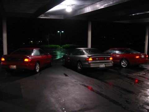 1996 Ford Probe - Three coupes are parked under a covered area at night, with wet pavement reflecting the lights.