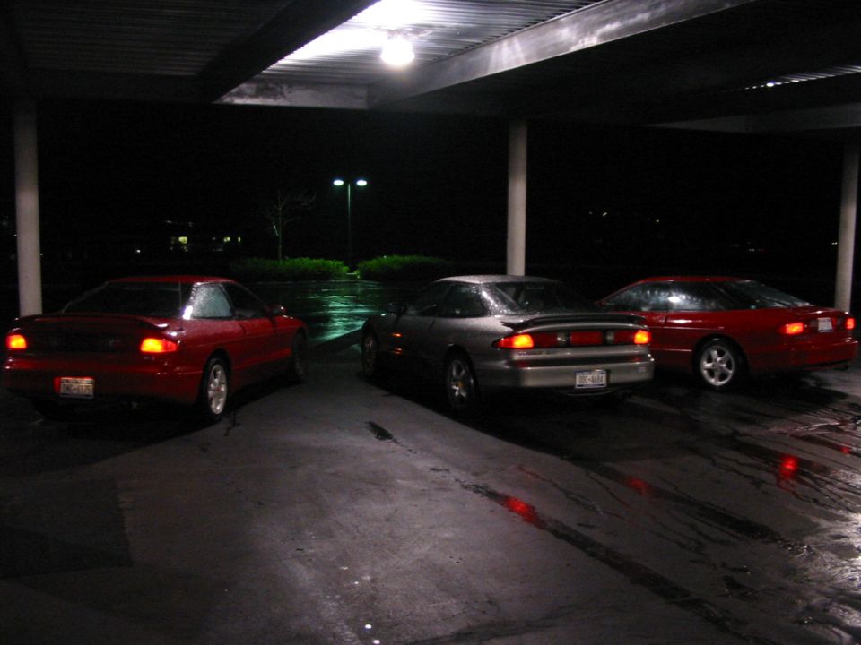 Three red and silver coupes parked under a covered area at night. The middle car is silver, the other two are red