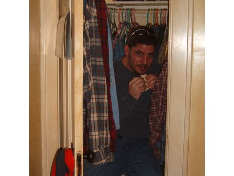 1993 Ford Bronco - A man is seen eating a sandwich while hiding in a closet filled with hanging clothes.