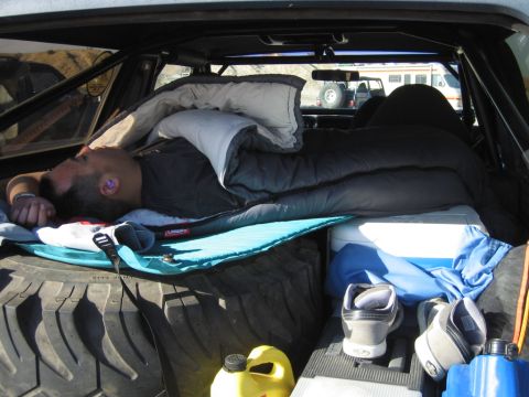 1985 Ford Bronco - Sleeping bag setup in the rear of an off-road vehicle, with another vehicle visible in the background.