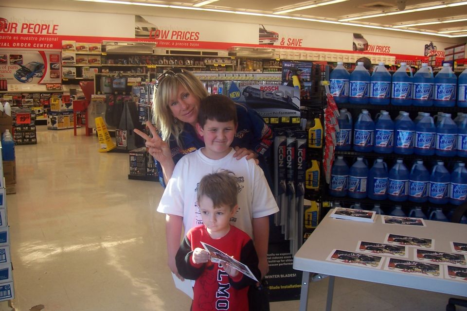 People posing in an auto parts store aisle with blue liquid jugs on shelves