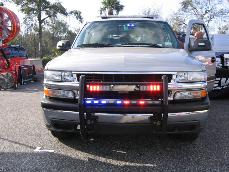 Front view of silver Chevy Tahoe police-style build with push bar, LED strobes, and roof light bar