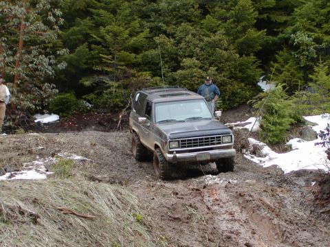 1987 Ford Bronco II - A Ford Bronco II navigates a challenging muddy terrain surrounded by dense forest.