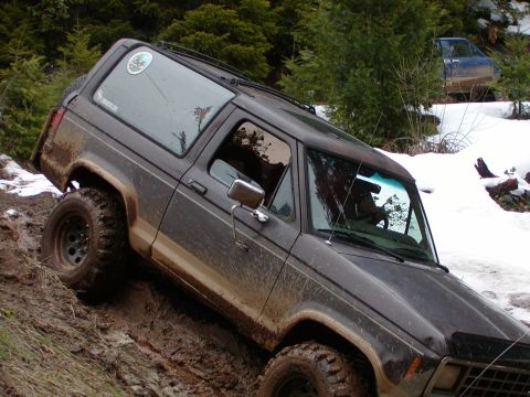 1987 Ford Bronco II - A 1987 Ford Bronco II navigates a challenging muddy terrain with snow visible in the surrounding woods.