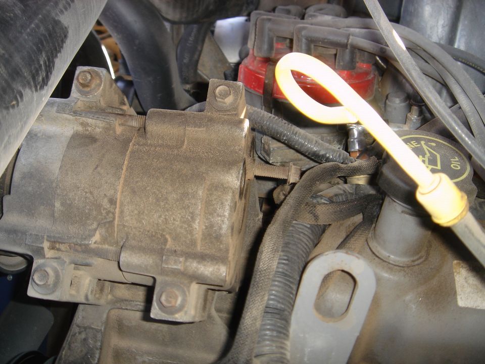 Engine bay close-up with dusty compressor, red distributor cap, yellow oil dipstick and engine oil filler cap.
