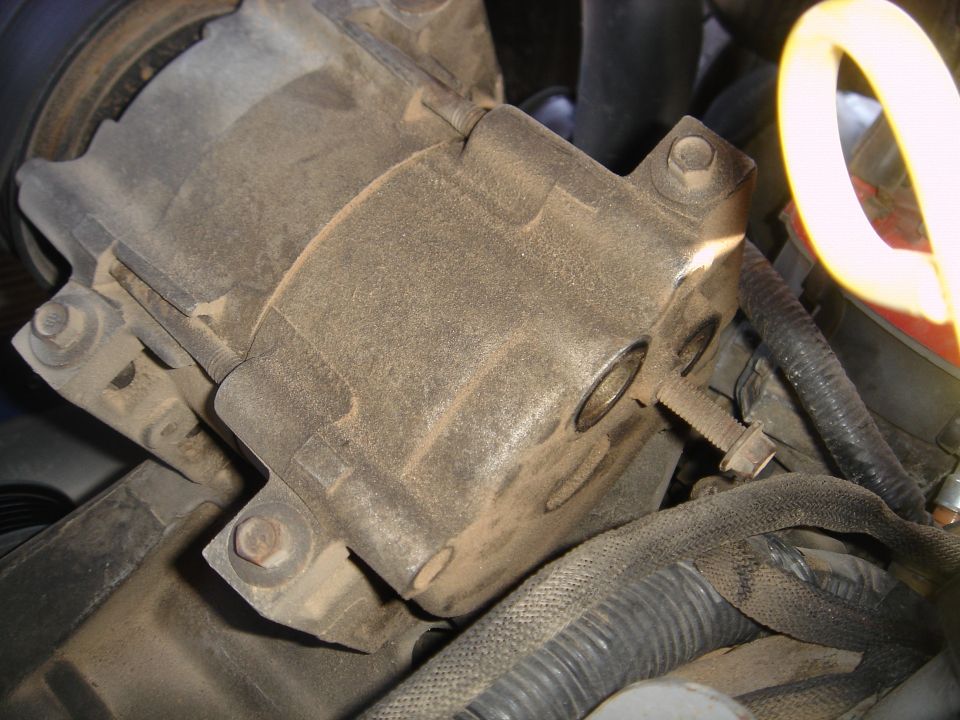 Dusty A/C compressor and mounting bracket in a Ford Bronco engine bay with wiring harness nearby