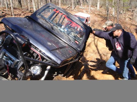 1978 Ford Bronco - Two men attempt to free a dark-colored off-road vehicle that is stuck in a muddy ditch, with another vehicle visible in the background.