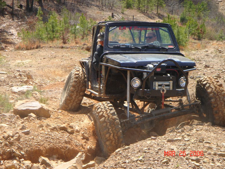 Modified off-road vehicle with large tires climbing a dirt obstacle. Winch visible on front