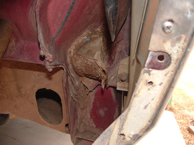 Caked mud and rust around a clogged cowl drain inside a red-painted vehicle body cavity