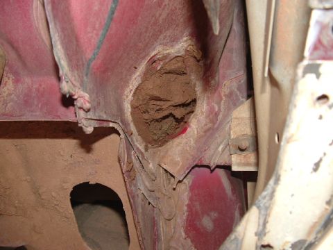 1990 Ford Bronco - A close-up view of a clogged drain hole on a vehicle's red metal body panel.