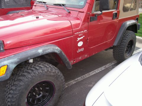 1998 Jeep TJ - Side view of a red 1998 Jeep TJ Wrangler 4.0L Sport model, a tan soft top and off-road tires.