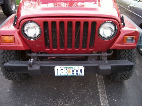 1998 Jeep TJ - This red Jeep Wrangler's front end is visible, its iconic grille and round headlights.