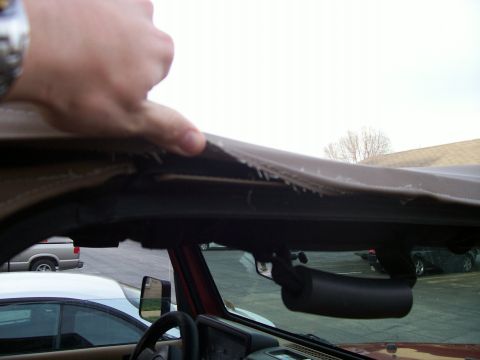 1998 Jeep TJ - A hand is shown pulling at a damaged soft top on the interior of a vehicle, with other cars in the background.