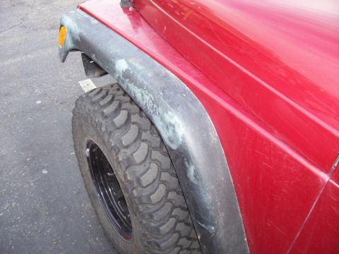 1998 Jeep TJ - Close-up of a red Jeep Wrangler's front fender and tire, showing wear on the fender flare.