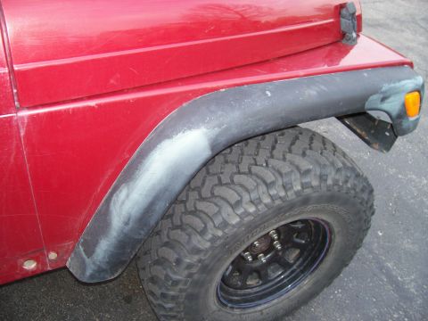 1998 Jeep TJ - The rear fender of a red Jeep shows some repair work on the fender flare, with a large off-road tire visible.