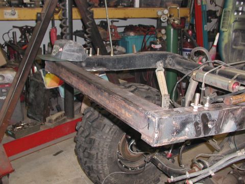 1989 Toyota Tacoma - The rear frame and suspension of a truck are shown in a workshop, with a large tire visible.