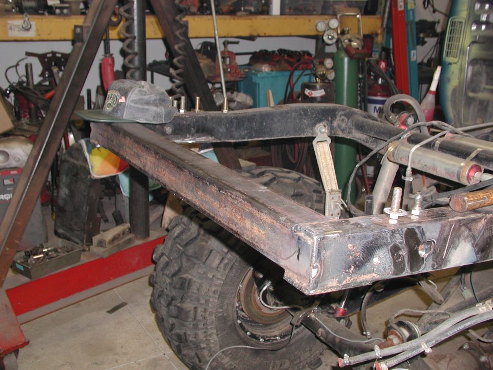 Truck frame with large tire and suspension components visible, in a workshop setting