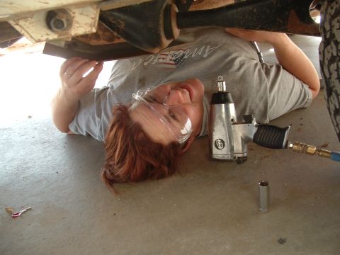 1990 Ford Bronco - Someone is working on the undercarriage of a vehicle, using an impact wrench and safety glasses.