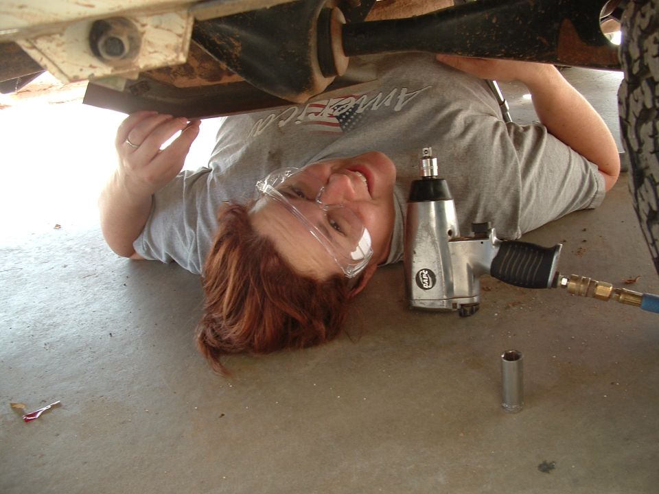 Person in safety glasses lying on the ground, working on the underside of a vehicle with an impact wrench
