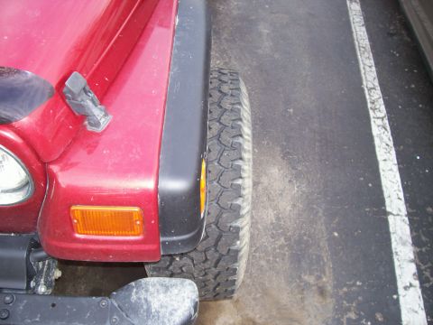 1998 Jeep TJ - Close-up of a red Jeep Wrangler's front fender and tire, showing the vehicle's characteristic body style.