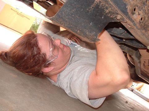 1990 Ford Bronco - A person works on the underside of a vehicle, with a box for an exhaust system visible.
