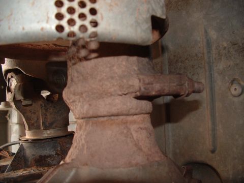 1990 Ford Bronco - Close-up view of a rusted exhaust pipe connection, partially obscured by a perforated heat shield.