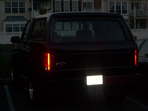 1982 Ford Bronco - The rear of a dark SUV is visible, with its license plate illuminated.