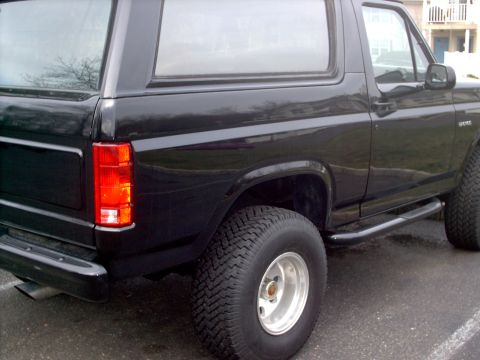 1982 Ford Bronco - Rear side view of a black SUV, a prominent tire and side step.