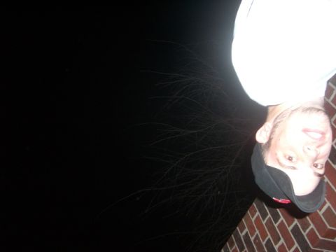 1985 Ford Bronco - Dark, upside-down flash snapshot of a person in a white t-shirt and dark cap standing on a brick surface at night, with most of the frame b…