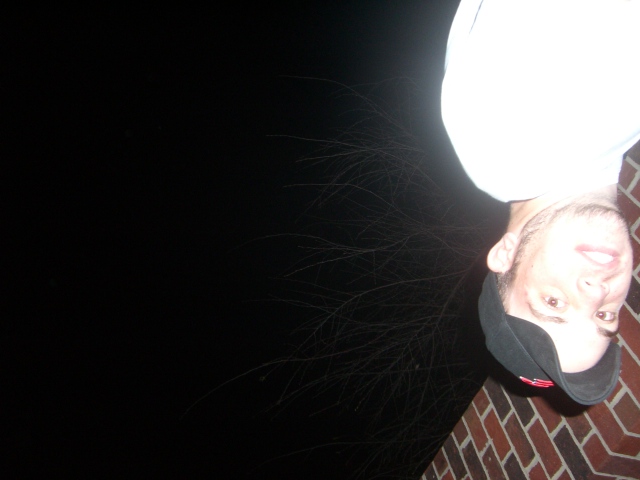 Upside-down night snapshot of a person in a white shirt and dark cap on brick