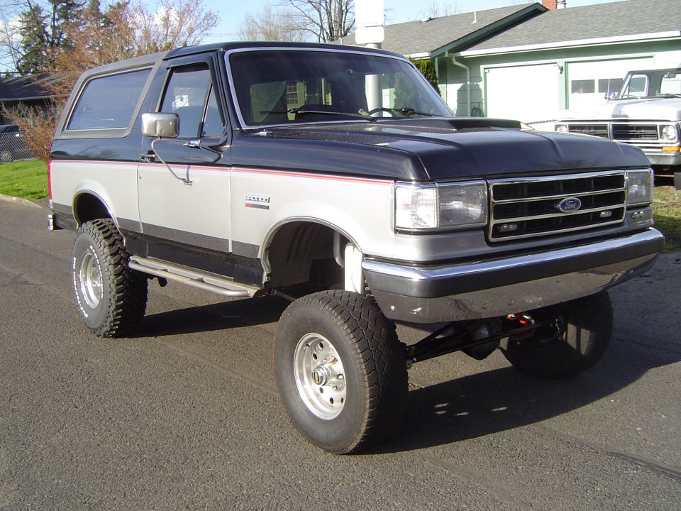 Lifted grey and silver Ford Bronco on white-spoke wheels parked on a street, front 3/4 view