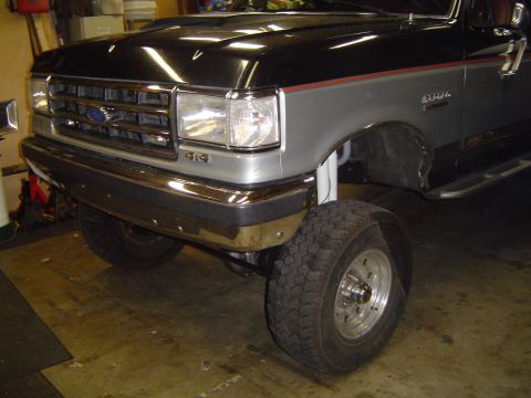 1989 Ford Bronco - This lifted Ford truck features a chrome grille and bumper, with a prominent 4x4 emblem.