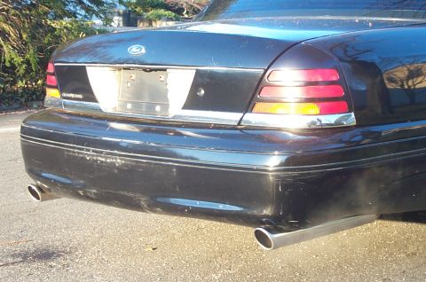 1999 Ford Crown Victoria - Close rear view of a black Ford Crown Victoria showing the trunk lid with the blue Ford oval, the empty license plate recess, and the red-a…