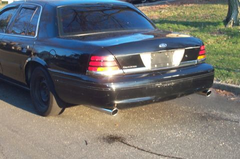 1999 Ford Crown Victoria - Three-quarter rear view of a black Ford Crown Victoria sedan parked on asphalt beside a grass verge, showing dual chrome-tipped exhaust out…