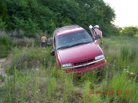 1989 Ford Bronco II - A red Chevrolet SUV is stuck in overgrown grass, with two men standing near it.