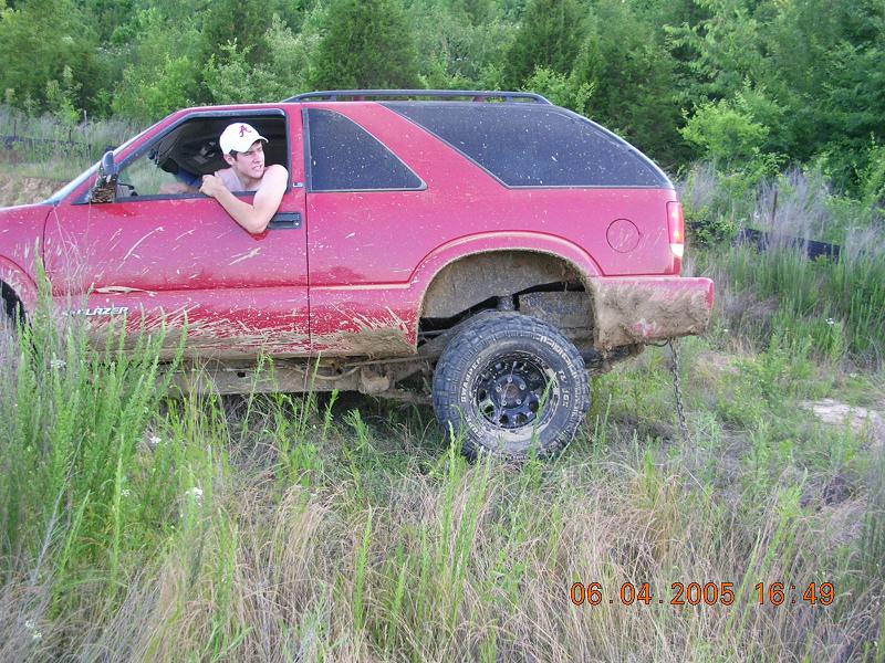Red SUV side view, covered in mud, with a person leaning out the window