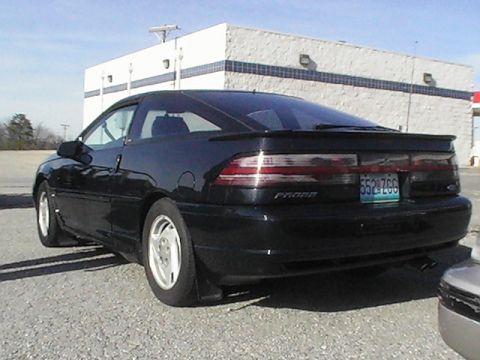 1994 Ford Probe - A black Ford Probe is parked in front of a building, showing its rear end and a spoiler.
