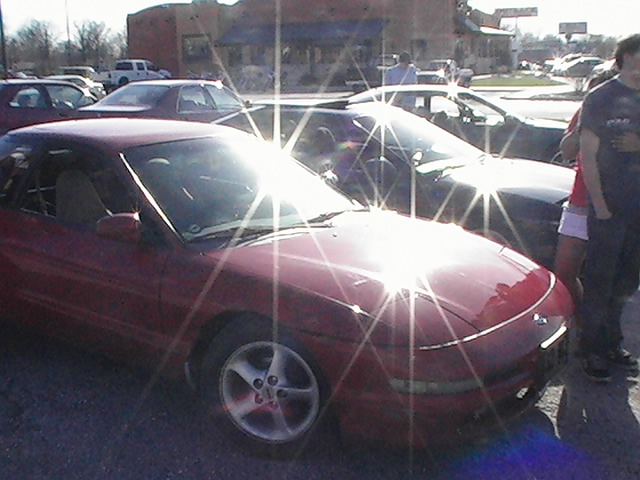 Red Ford Probe coupe on silver five-spoke wheels at a sunlit car meet parking lot