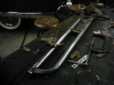 1978 Ford Bronco - A pair of bent and welded steel tube bars, a fabricated nerf bar or side-step assembly, laid out on a dark shop workbench with C-clamps, ta…