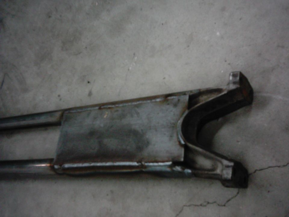 Metal radius arm with a welded bracket and rubber bushing, resting on a concrete floor