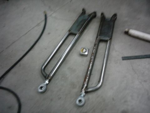 1978 Ford Bronco - Two custom radius arms are laid out on a workshop floor next to a tape measure.